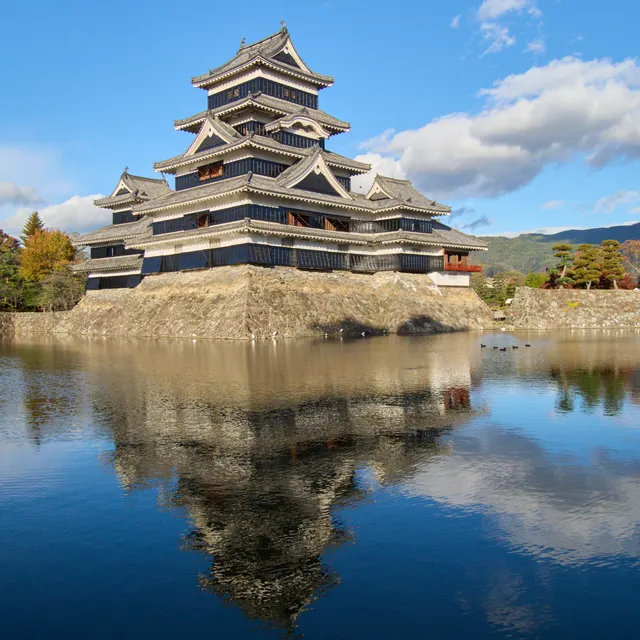 Matsumoto Castle keep reflected in the moat with autumn leaves and blue sky