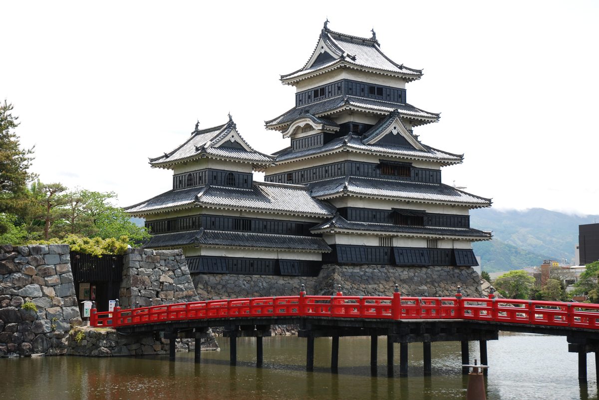 Matsumoto Castle's black main keep and smaller north-west keep above the moat, with the red Uzumibashi bridge in front
